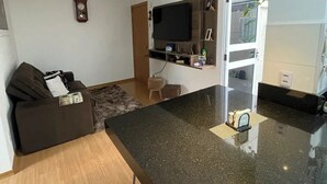 Une cuisine moderne avec un plan de travail noir, un téléviseur encastré et un petit tabouret.
