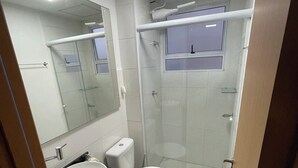 Une petite salle de bain comprenant un lavabo, des toilettes et une douche fermée par une paroi de verre.
