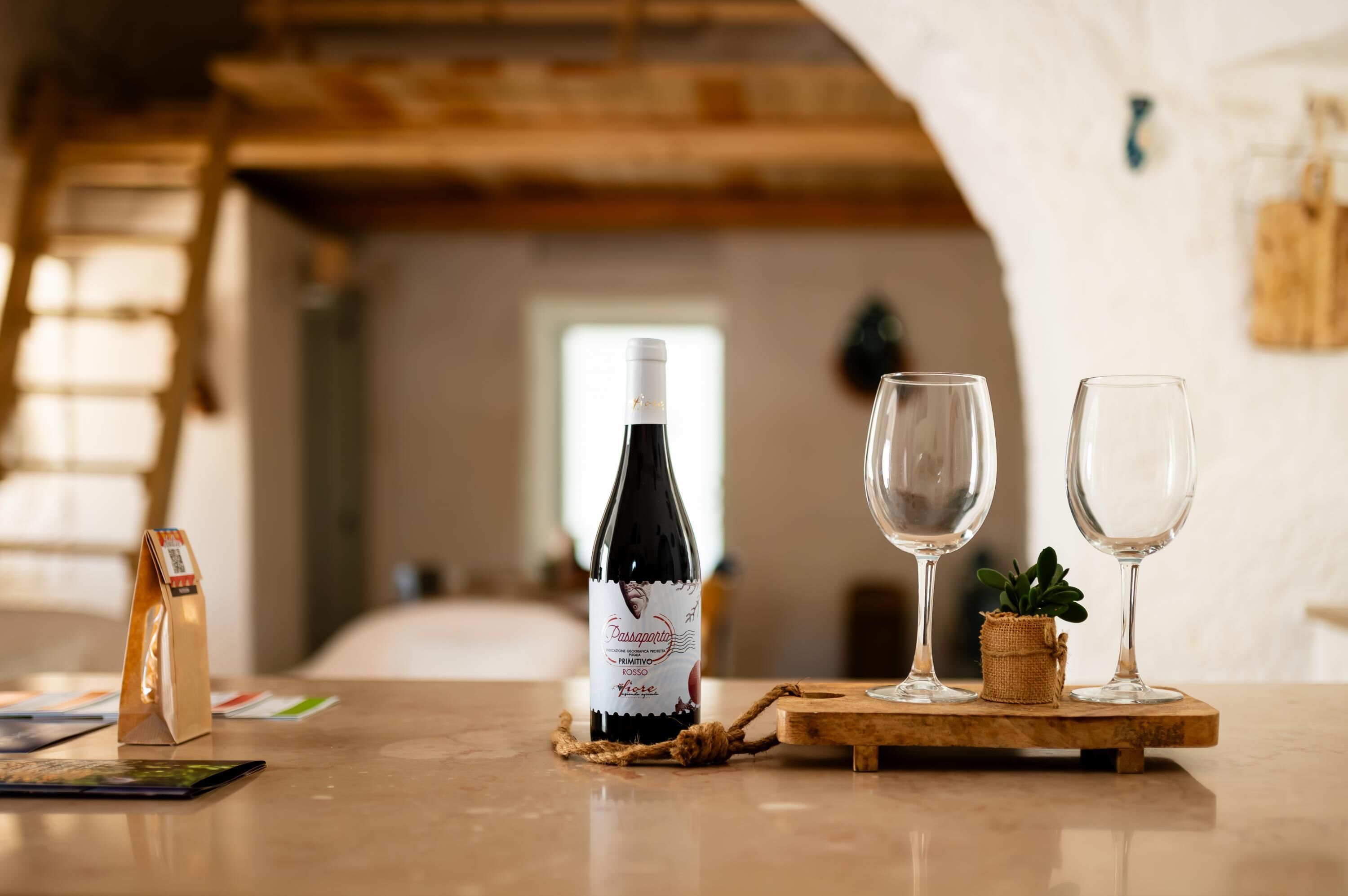 A bottle of wine on a wooden coaster with two empty wine glasses on a table.