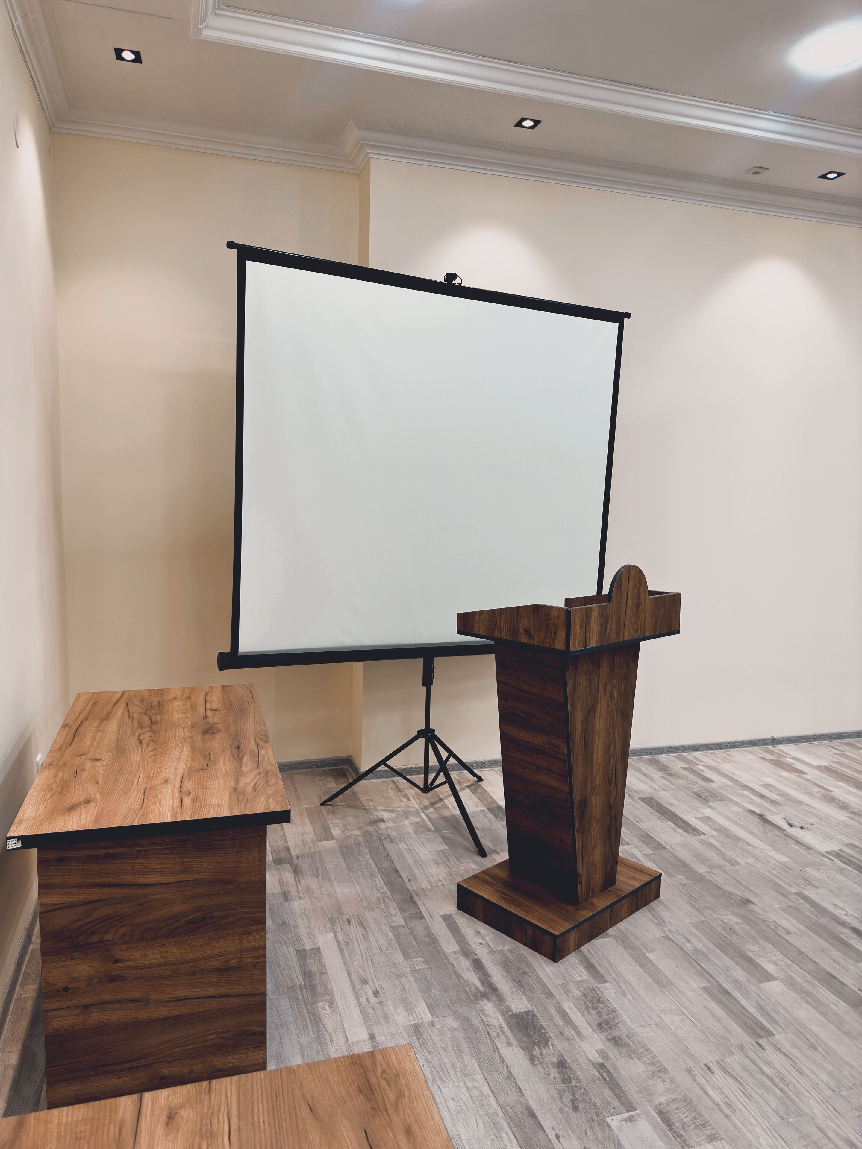 A conference room with a wooden table, a podium, and a projection screen.