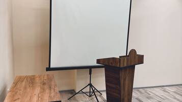 Un salón de conferencias con una mesa de madera, un atril y una pantalla de proyección.