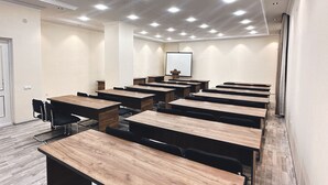 Een congreszaal met meerdere tafels en stoelen, inbouwspots en een projectiescherm.