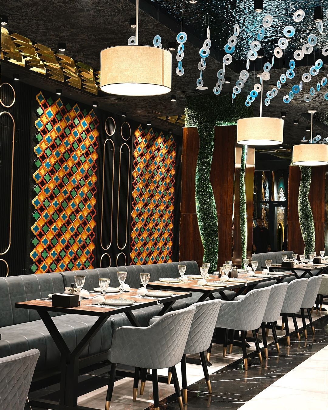 A restaurant with a long dining table, multiple chairs, and hanging pendant lights.