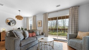A modern living room with a grey sofa, a round coffee table, and a large window with curtains. - Lakeside 1bd Condo with King bed Close to it all! (Branson)