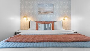 A neatly arranged bedroom with a patterned wallpaper, a painting above the bed, and two wall-mounted lamps. - Lakeside 1bd Condo with King bed Close to it all! (Branson)