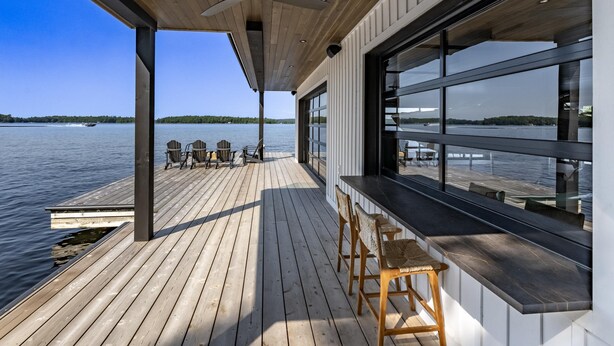 Una terraza de madera con una zona de bar, sillas y vistas al agua.