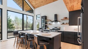 Eine moderne Küche mit einer großen Kochinsel, Barhocker und Blick auf den Wald.