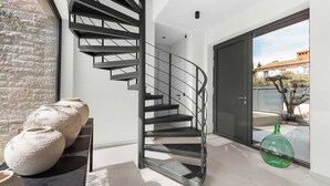 Ein modernes Interieur mit einer Wendeltreppe, einer Steinwand und einem großen Fenster mit Blick auf ein Gebäude und Bäume.