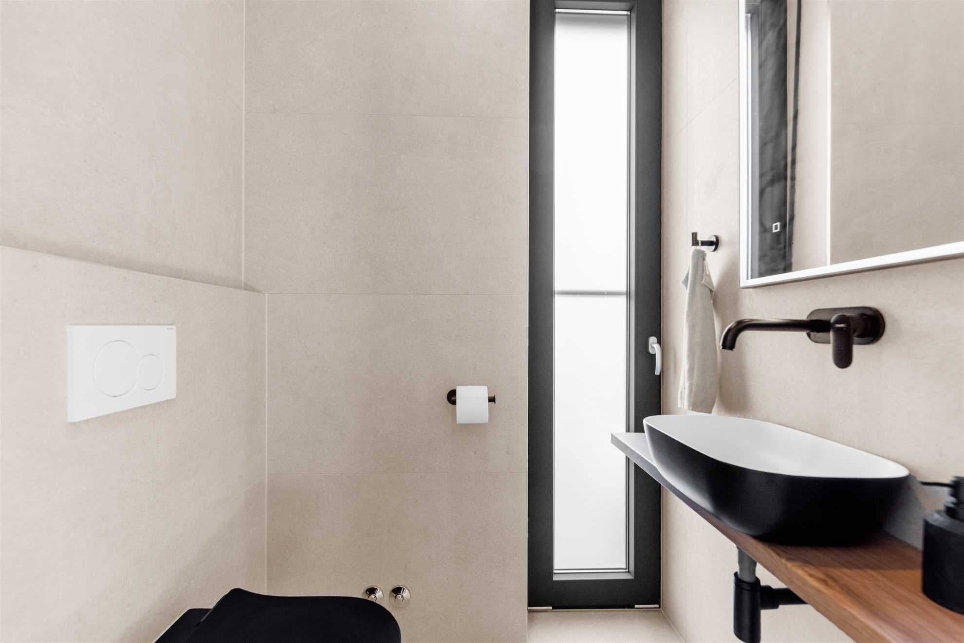 Une salle de bain moderne avec un lavabo noir, un miroir et des toilettes.