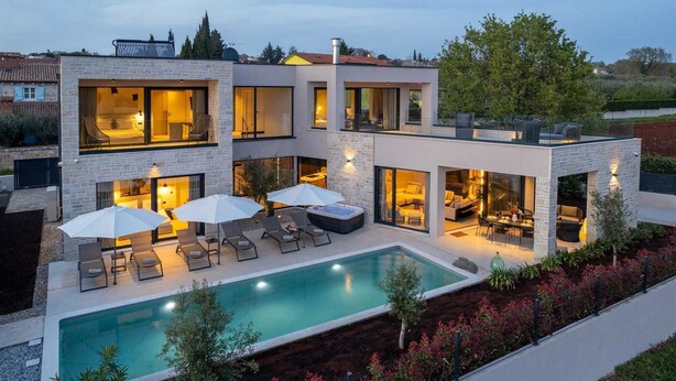 Ein modernes, zweistöckiges Haus mit Swimmingpool, Sitzgelegenheiten im Freien und großen Fenstern.