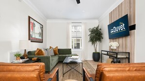 A modern living room with a sectional sofa, leather armchairs, a coffee table, and a flat-screen TV mounted on a wooden wall. - 1 Block to Historic King St | The Place to Be (Charleston)