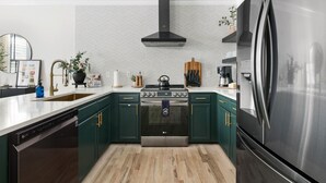 A modern kitchen with dark green cabinets, a stainless steel refrigerator, a black range hood, and a herringbone-patterned backsplash. - 1 Block to Historic King St | The Place to Be (Charleston)