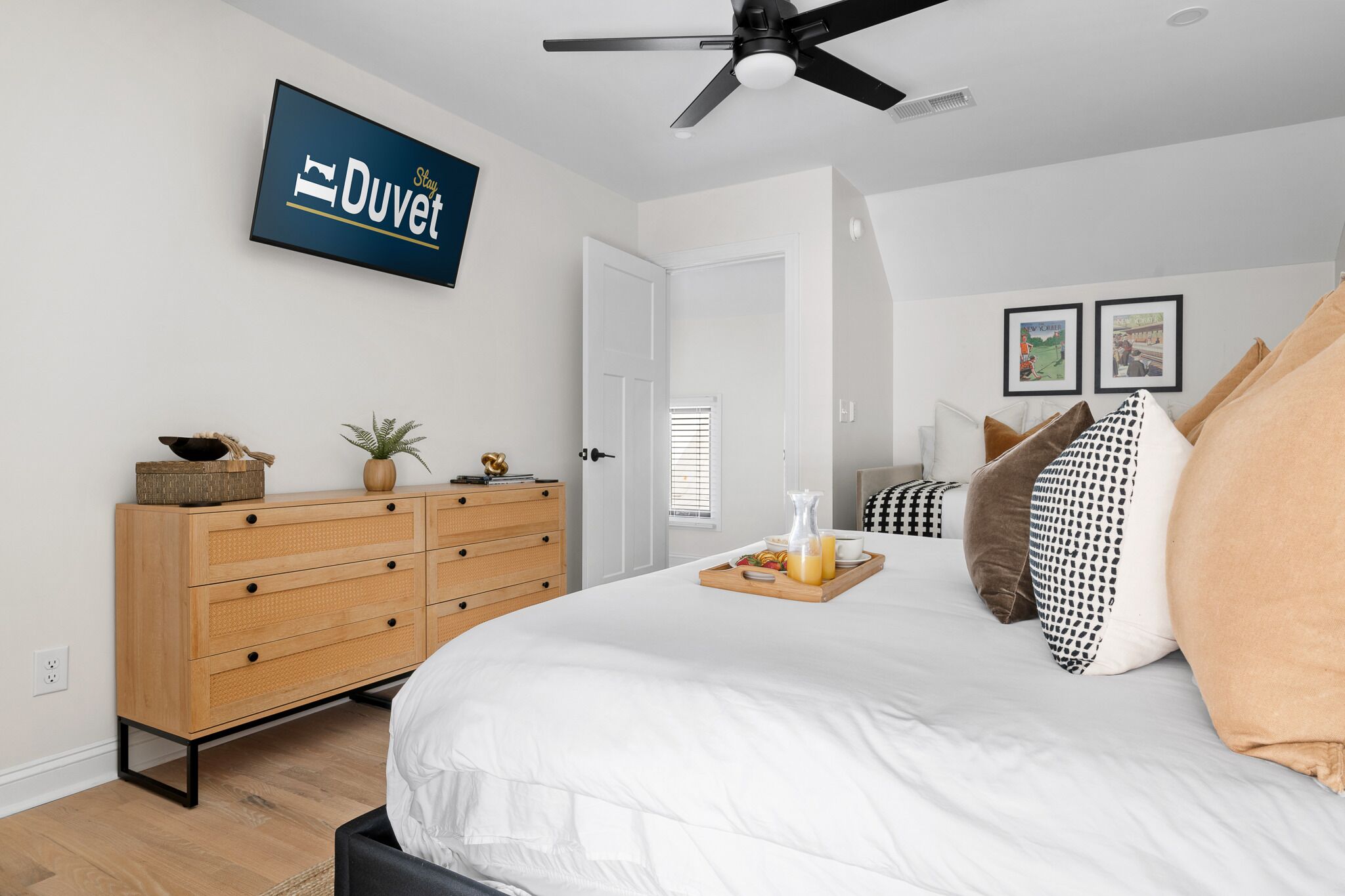 A bedroom with a bed, a wooden dresser, a ceiling fan, and a wall-mounted TV displaying 'Stay Duvet'.