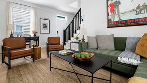 A living room with a green sofa, two brown armchairs, a black coffee table, and a framed poster on the wall. - 1 Block to Historic King St | The Place to Be (Charleston)