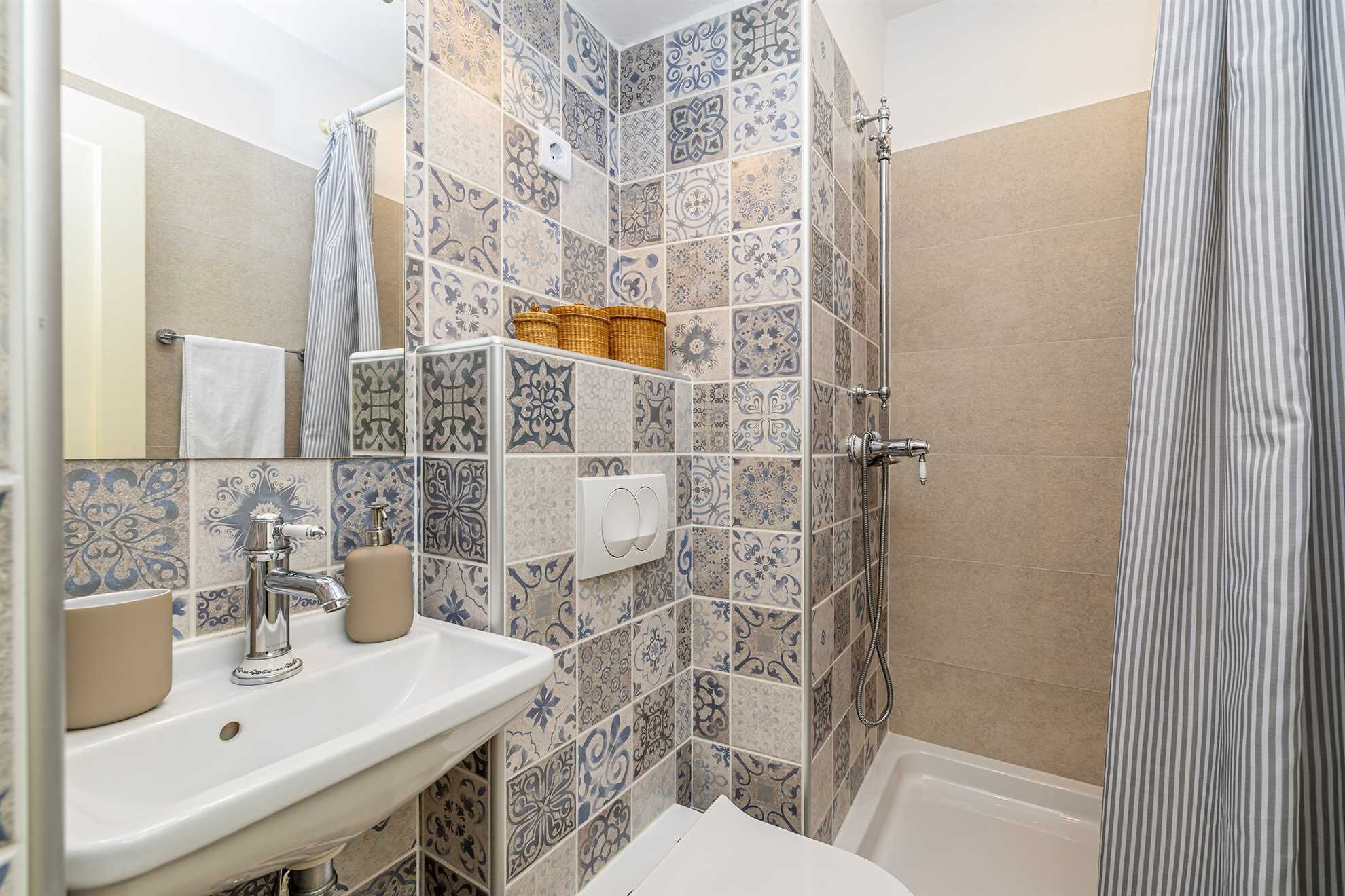 Un baño con lavamanos, espejo, ducha y azulejos estampados.