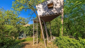 A treehouse with a ladder, surrounded by dense foliage.