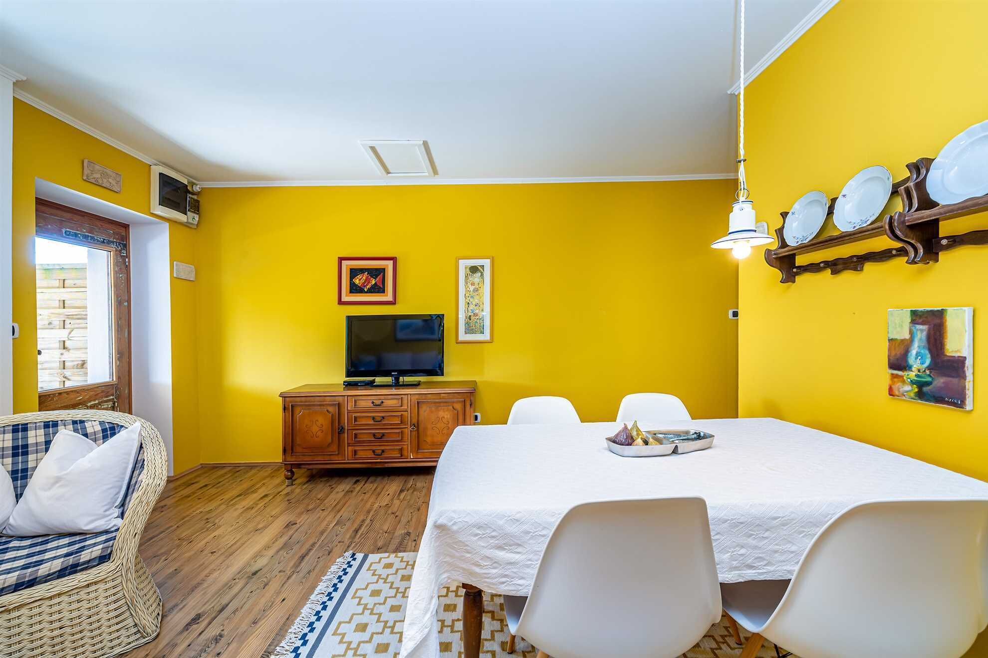 A dining area with a table set for four, a television, and a wooden cabinet.