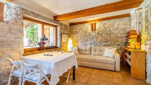 A stone-walled room with a wooden ceiling, a beige sofa, a dining table with chairs, and a wooden cabinet with decorative items.