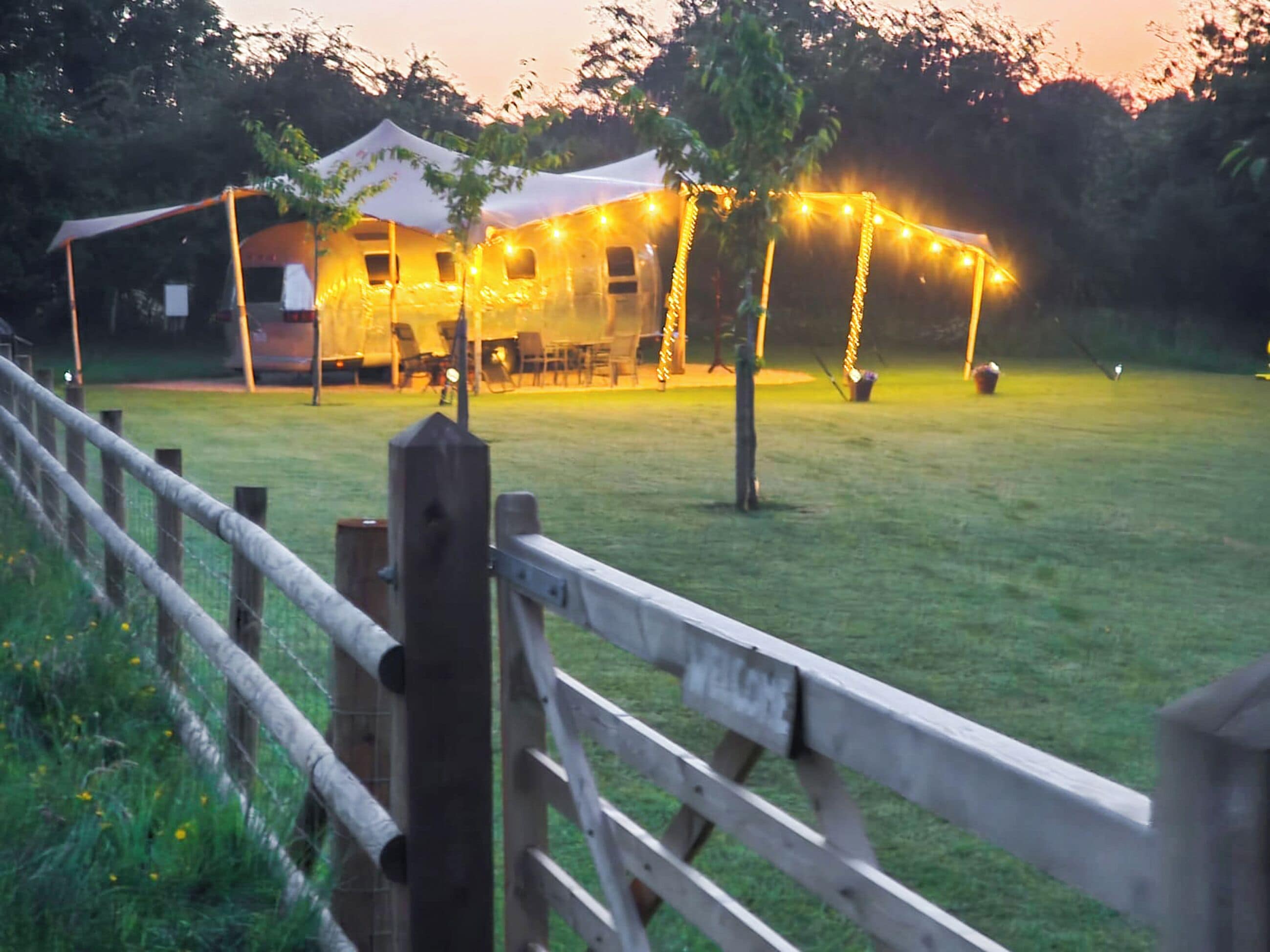 A tented outdoor area with string lights, a wooden fence, and a grassy field.