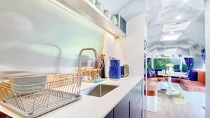 Une cuisine moderne équipée d’un évier, d’un égouttoir et d’un plan de travail. On aperçoit un coin repas avec une table et des chaises à travers une cloison en verre.