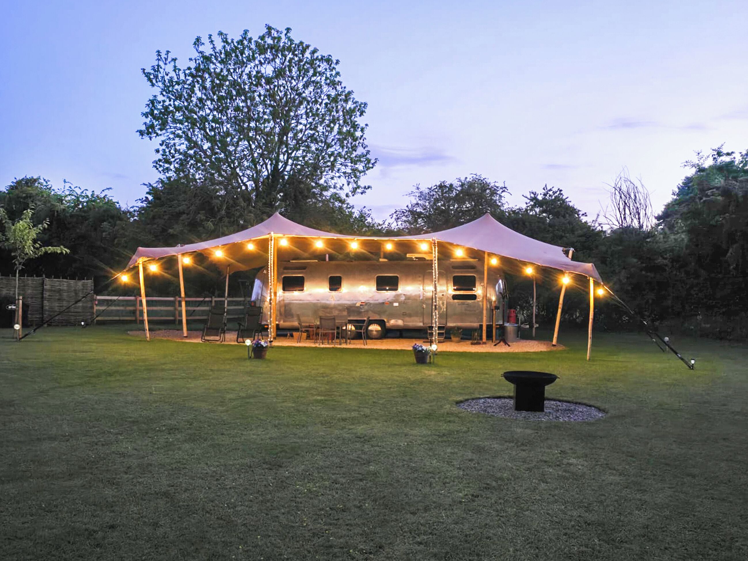 Zona exterior coberta amb espai de menjador, una barbacoa i una tenda amb llums penjants.