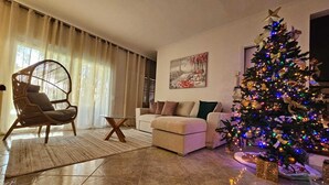 Ein Wohnzimmer mit einem großen Weihnachtsbaum, einem Korbstuhl, einer Couch und einem Gemälde an der Wand.