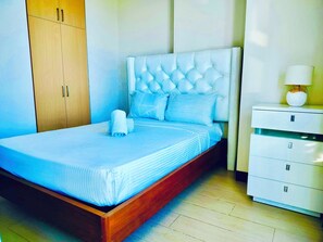 A neatly made bed with a tufted headboard, a wooden wardrobe, and a bedside table with a lamp. - Luxury 1BR 55sqm 1 Pacific MactanNewtown (Lapu-Lapu)