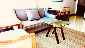 A living room with a sofa, a glass coffee table, a patterned rug, and a dining area with chairs and a table. - Luxury 1BR 55sqm 1 Pacific MactanNewtown (Lapu-Lapu)