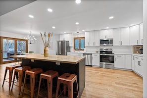Una cocina moderna con armarios blancos, electrodomésticos de acero inoxidable y una isla central con taburetes.