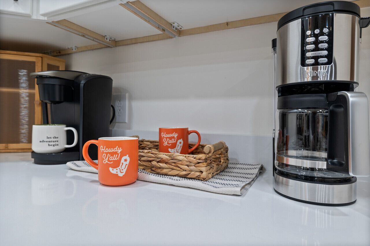 Una zona de cocina con cafetera, dos tazas y una cesta de mimbre.