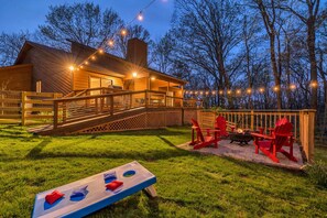 A wooden cabin with a deck, outdoor seating, and a fire pit.
