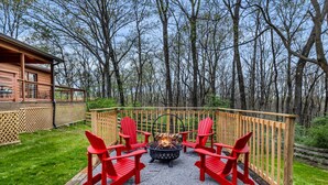 Eine Terrasse mit Feuerstelle und roten Stühlen, umgeben von einem Holzzaun und Bäumen.