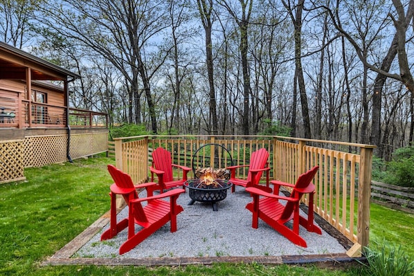 Eine Terrasse mit Feuerstelle und roten Stühlen, umgeben von einem Holzzaun und Bäumen.