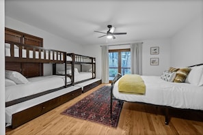 A bedroom with a bunk bed, a single bed, a ceiling fan, and a window with curtains.