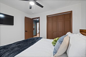 Ein Schlafzimmer mit Bett, Deckenventilator, an der Wand montiertem Fernseher und einem Schrank mit Spiegel.