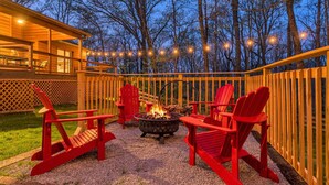 An outdoor deck with red Adirondack chairs, a fire pit, and string lights.