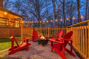 Une terrasse extérieure avec des fauteuils Adirondack rouges, un foyer et des guirlandes lumineuses.