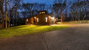A wooden cabin with a garage, surrounded by trees and a gravel driveway.