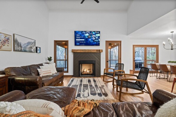 A spacious living room with a fireplace, leather sofas, a flat-screen TV, and a dining area with chairs.