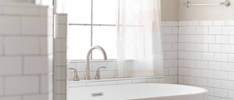 A modern bathroom with a freestanding bathtub, a window with a curtain, and a towel rack.