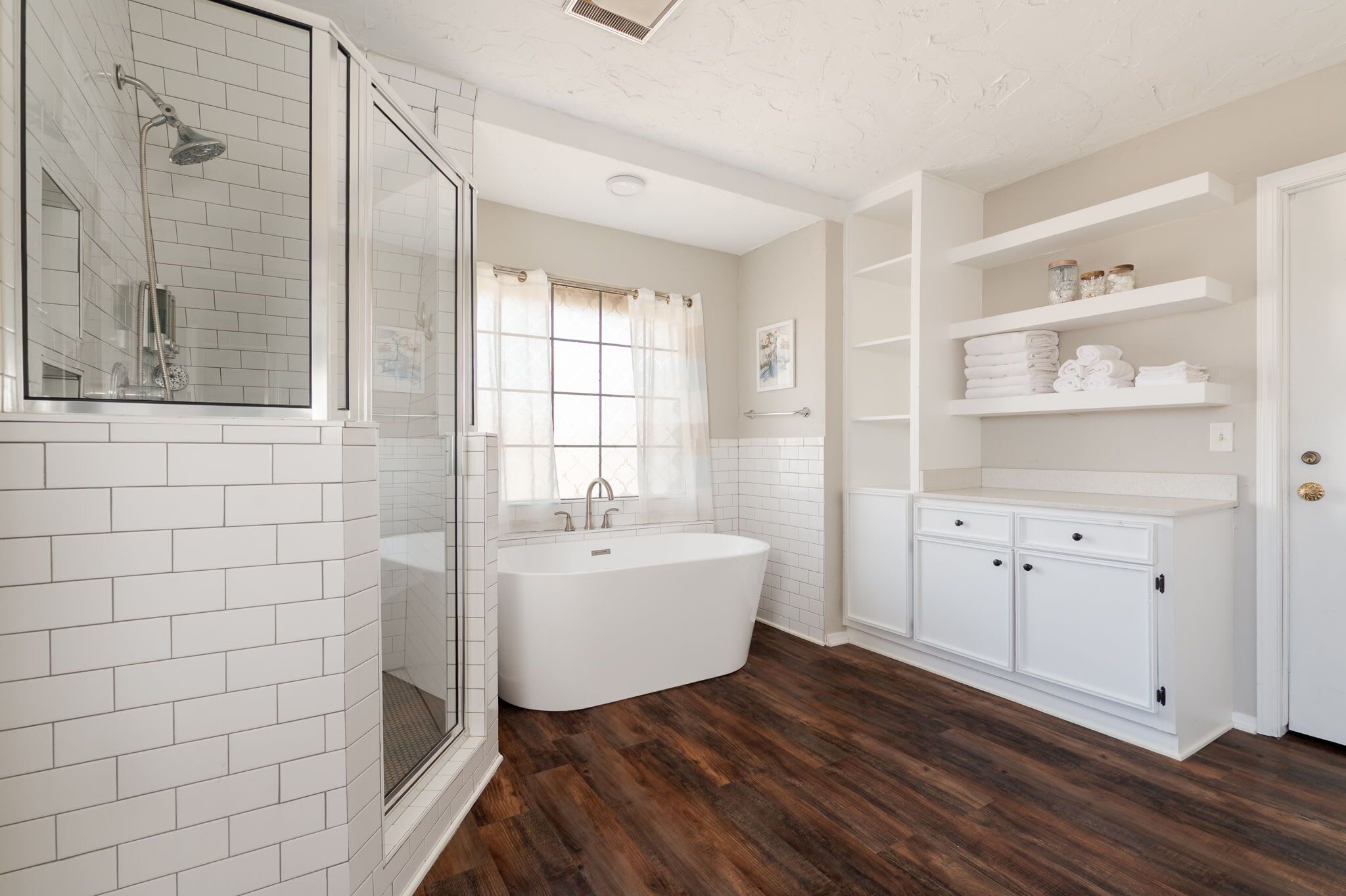 A modern bathroom with a freestanding bathtub, a glass-enclosed shower, and white cabinetry with shelves.