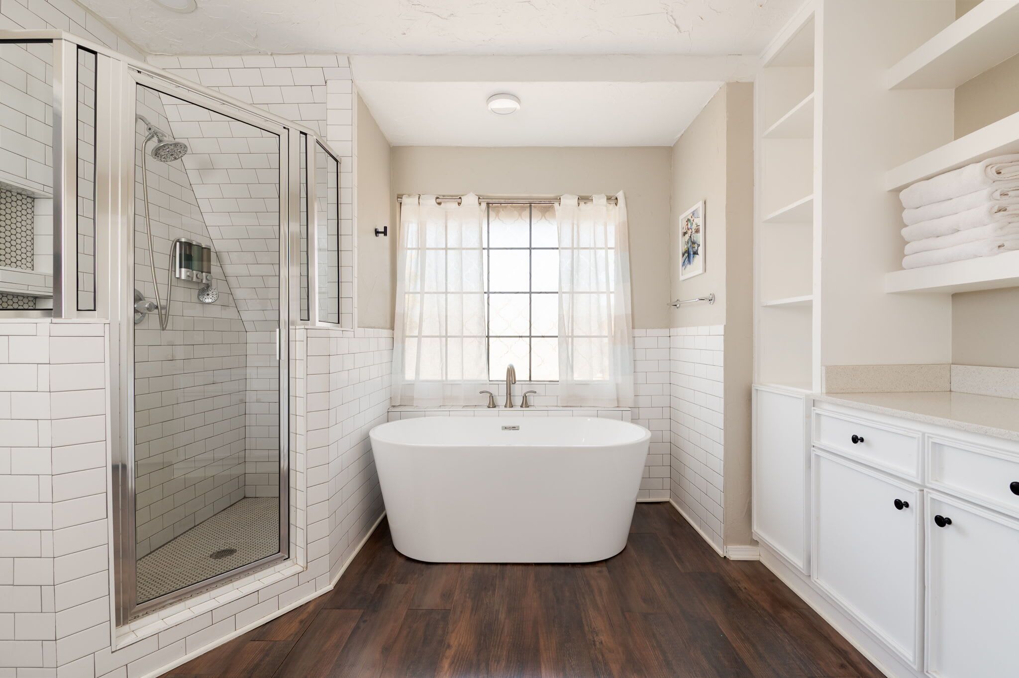 A modern bathroom with a freestanding bathtub, a glass-enclosed shower, and white tiled walls.