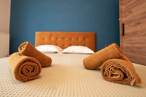A bed with a tufted headboard, white pillows, and rolled towels on a textured bedspread.