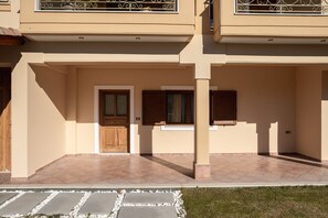 A two-story building with a beige facade, a tiled entrance, and a small balcony with metal railings.