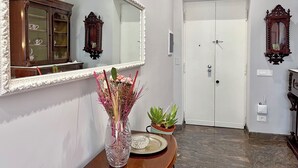 A hallway with a white door, a mirror, a cabinet, and a vase with flowers. - 4BNB - Leone IV Apartment (Rome)