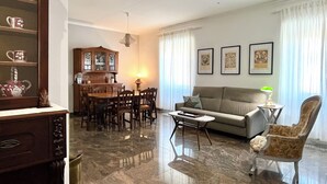 A living room with a sofa, coffee table, dining table, chairs, and a cabinet. - 4BNB - Leone IV Apartment (Rome)