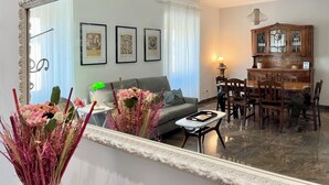 A living room with a sofa, a coffee table, and a dining area with wooden chairs and a cabinet. - 4BNB - Leone IV Apartment (Rome)
