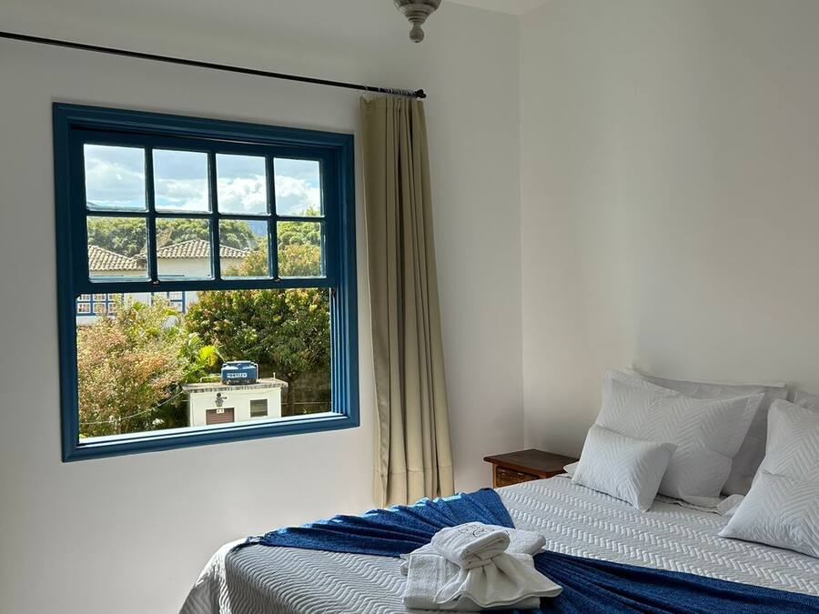 Un dormitorio con cama, ventana que da a zonas verdes y una araña.