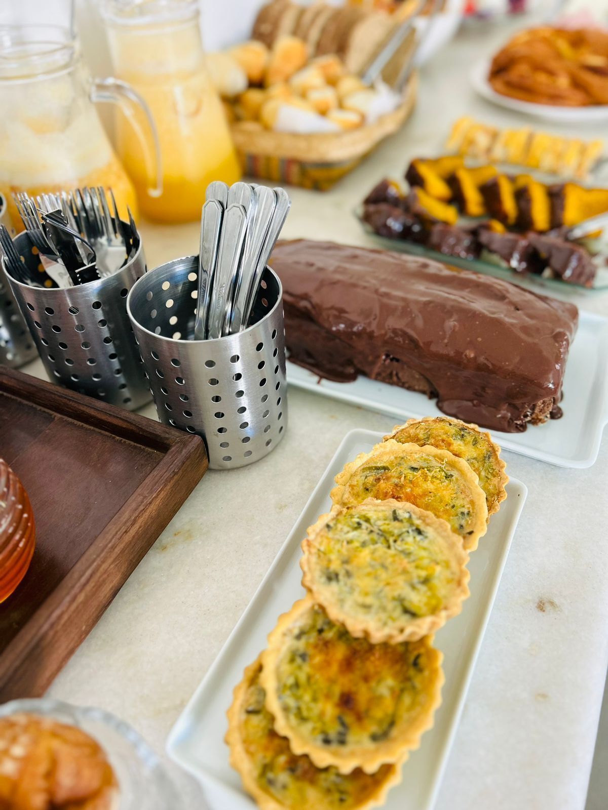 A breakfast buffet with various food items including quiches, chocolate desserts, and a fruit basket.