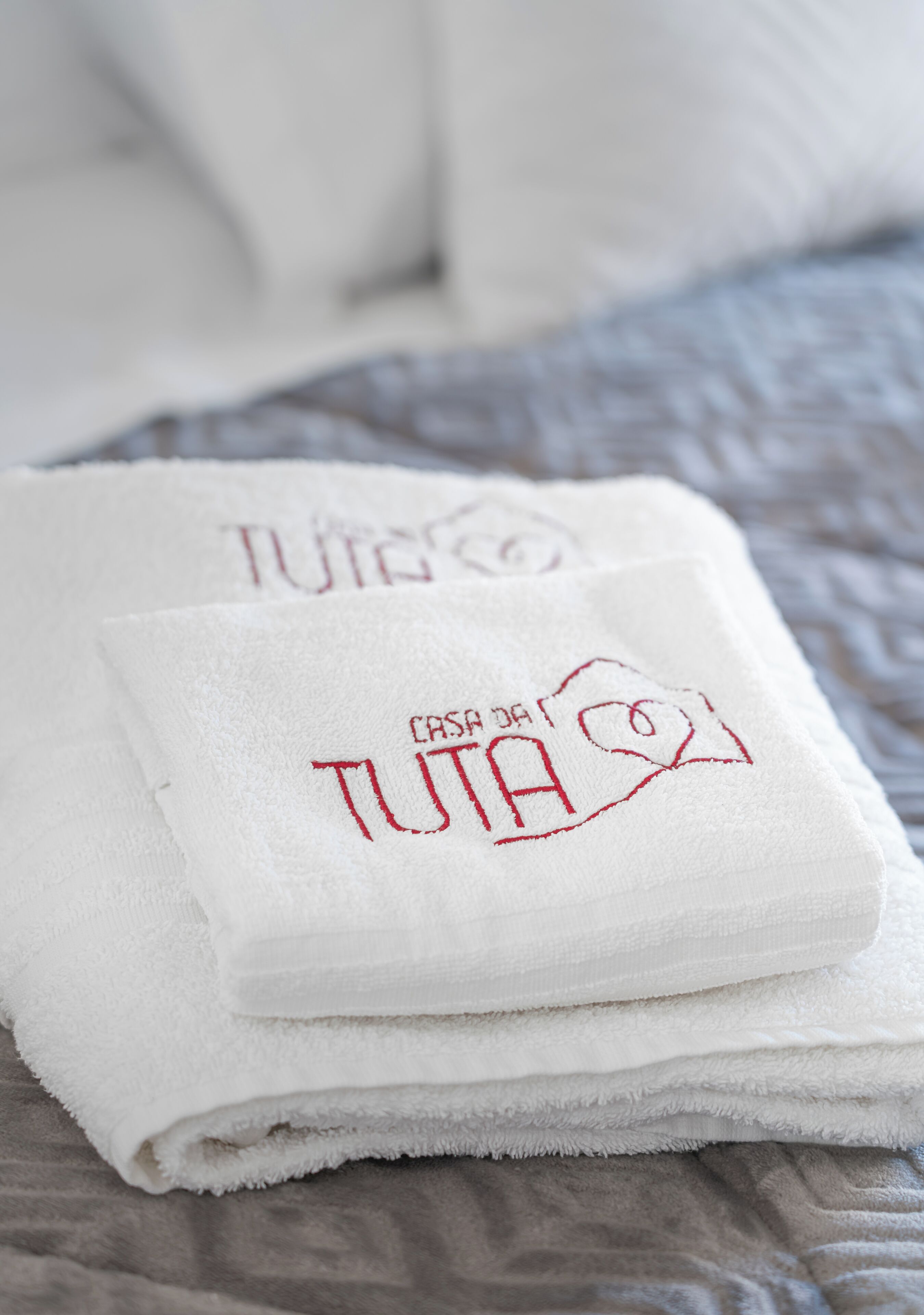 A neatly folded white towel with embroidered text on a bed.